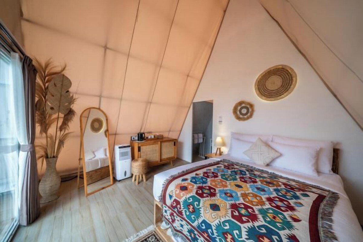 A cozy bedroom with a sloped ceiling, a colorful bedspread, a bedside table with a lamp, and a decorative wall hanging.