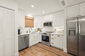 A modern kitchen with white cabinets, stainless steel appliances, and a wooden floor. - Walk to Lido Beach & St. Armands! Heated Pool/Spa (Sarasota)