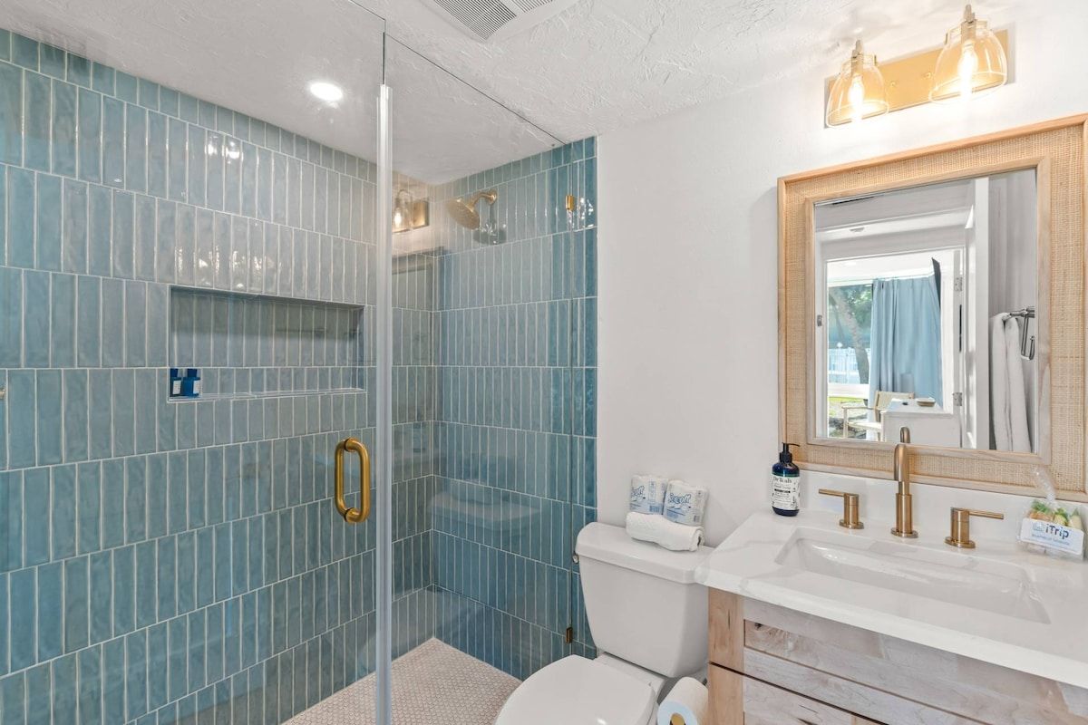 A bathroom with a glass-enclosed shower, a white toilet, and a sink with a mirror above it.