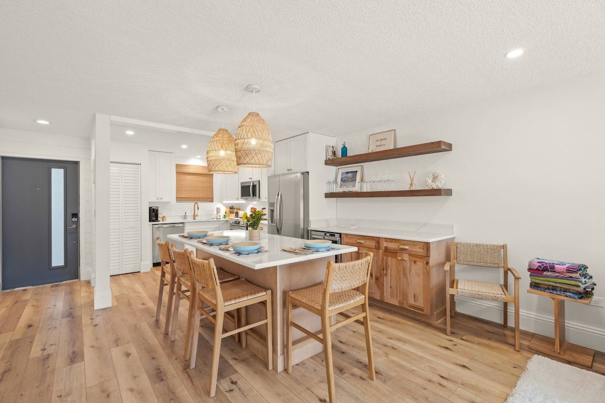 A modern kitchen with wooden flooring, a central island, and pendant lighting.