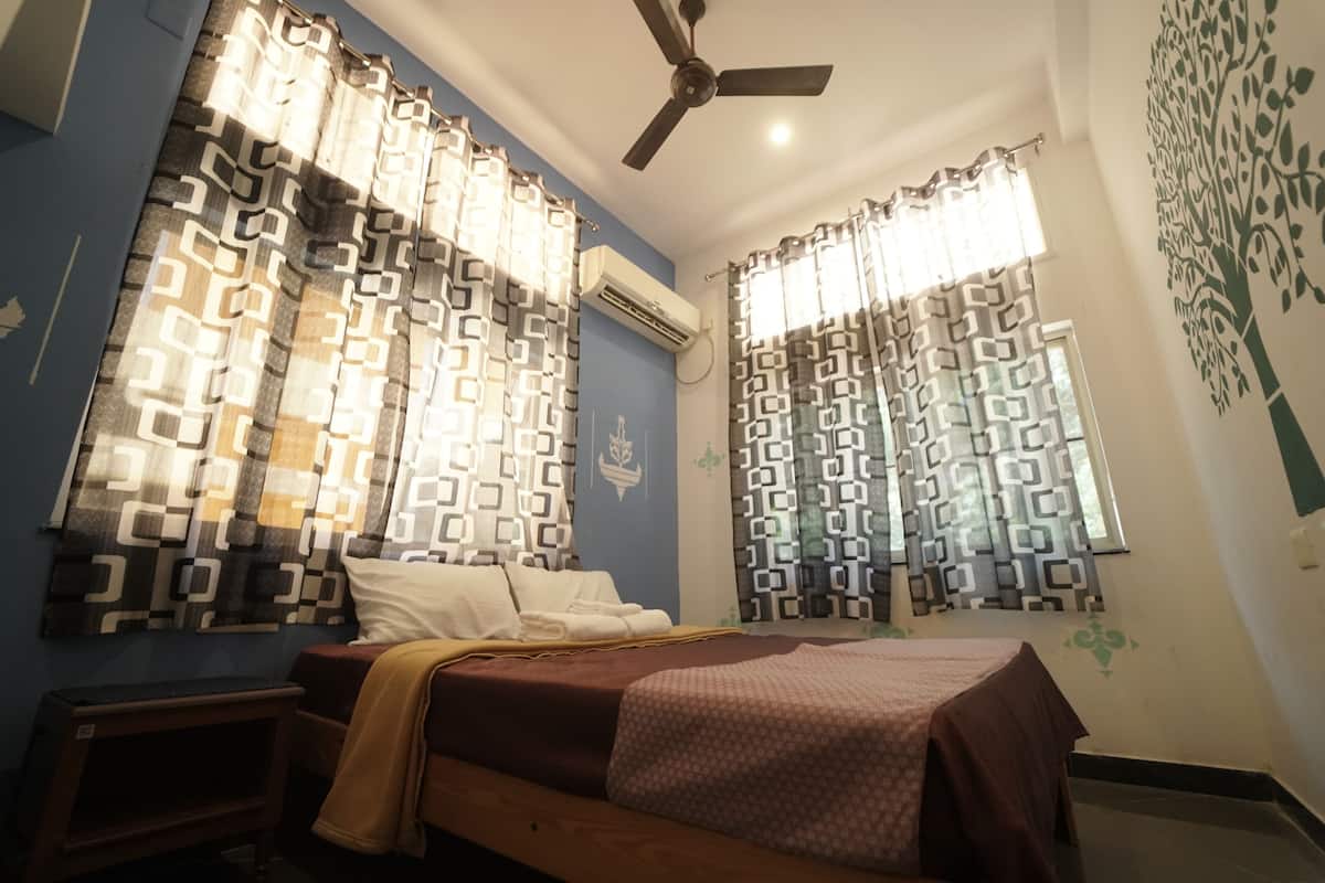 Une chambre à coucher avec un lit, un ventilateur de plafond, des rideaux à motifs et un élément décoratif mural.