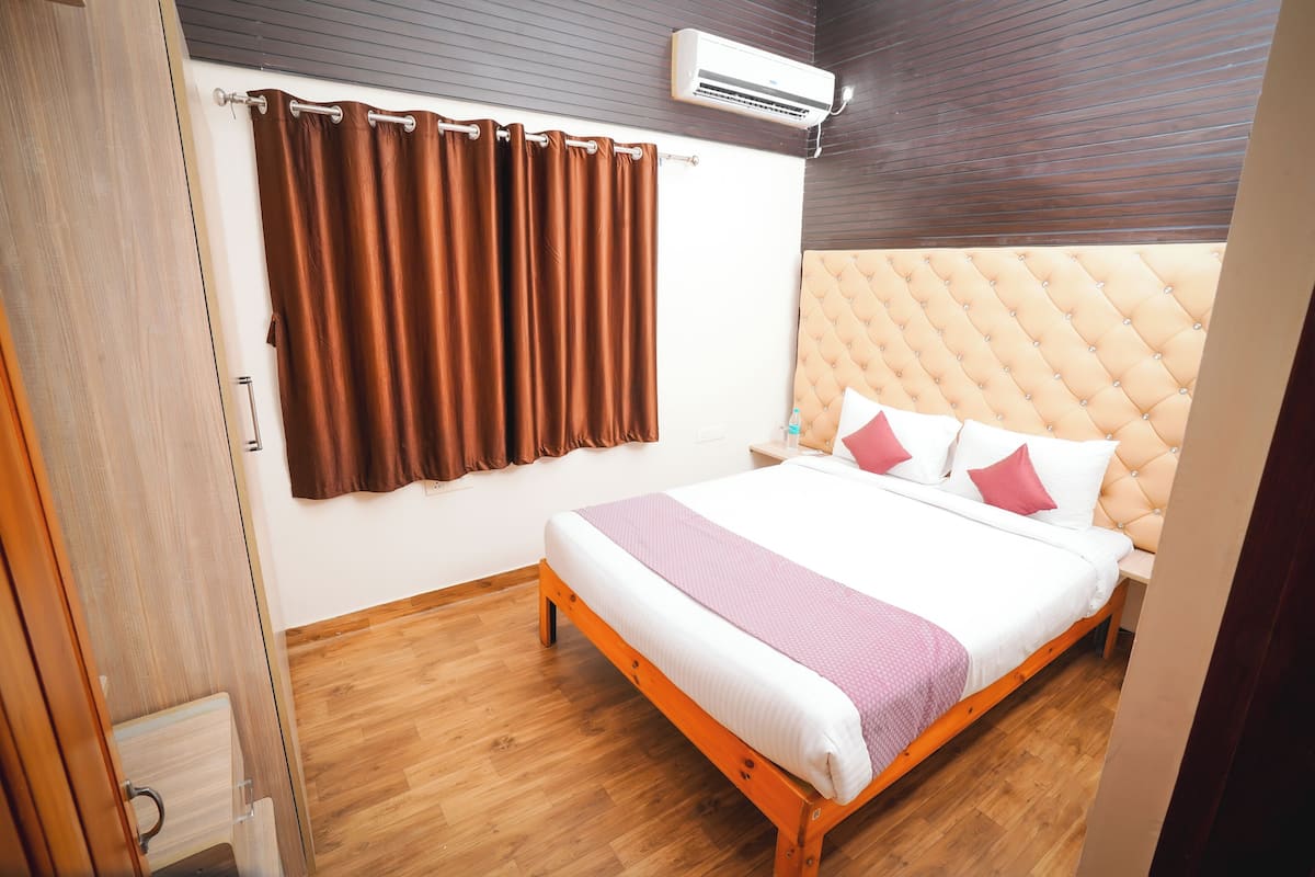 Une chambre avec un lit en bois, des rideaux marron, un climatiseur blanc et un plancher en bois.