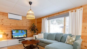 Un salon chaleureux avec un canapé d’angle, un plafond en bois, un téléviseur et un luminaire suspendu.