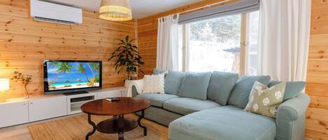 A cozy living room with a sectional sofa, a television, a wooden ceiling, and a large window.