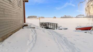 A snow-covered landscape with a wooden house, a snow-covered deck, and a red boat.