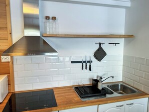 A kitchen with white subway tiles, a stainless steel range hood, a black induction cooktop, a sink with a faucet, and a hanging pot holder. - Brofeldt by Interhome (Tohmajärvi)