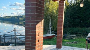 Une terrasse en bois avec un pilier en briques, donnant sur un lac paisible et entourée de verdure.
