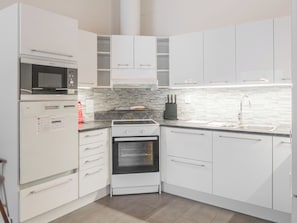 Une cuisine moderne avec des meubles blancs, un four encastré, un four à micro-ondes et un évier en acier inoxydable.