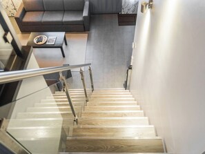 A modern interior with a staircase leading to a lower level, a grey sofa, and a small table with a magazine.