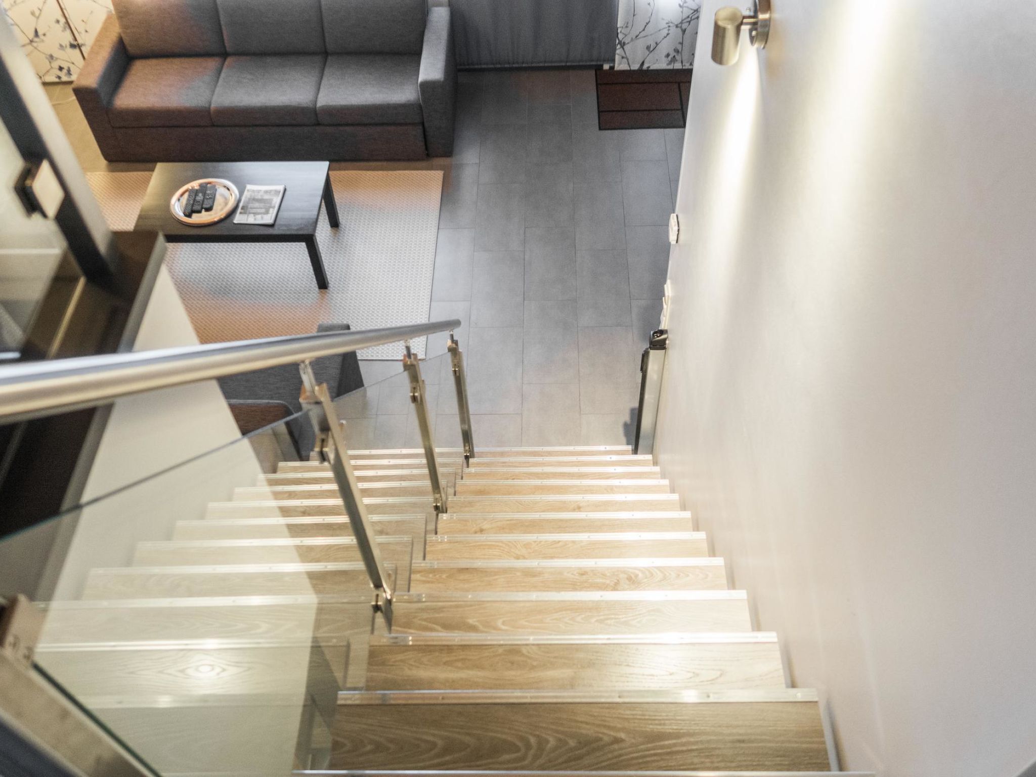 A modern staircase with wooden steps and metal railings, leading to a living area with a grey sofa and a coffee table.