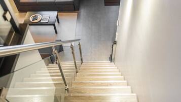 A modern staircase with wooden steps and metal railings, leading to a living area with a grey sofa and a coffee table.
