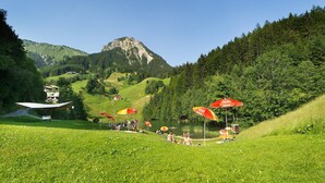 Un'area panoramica all'aperto con un lago, ombrelloni rossi e una montagna sullo sfondo.