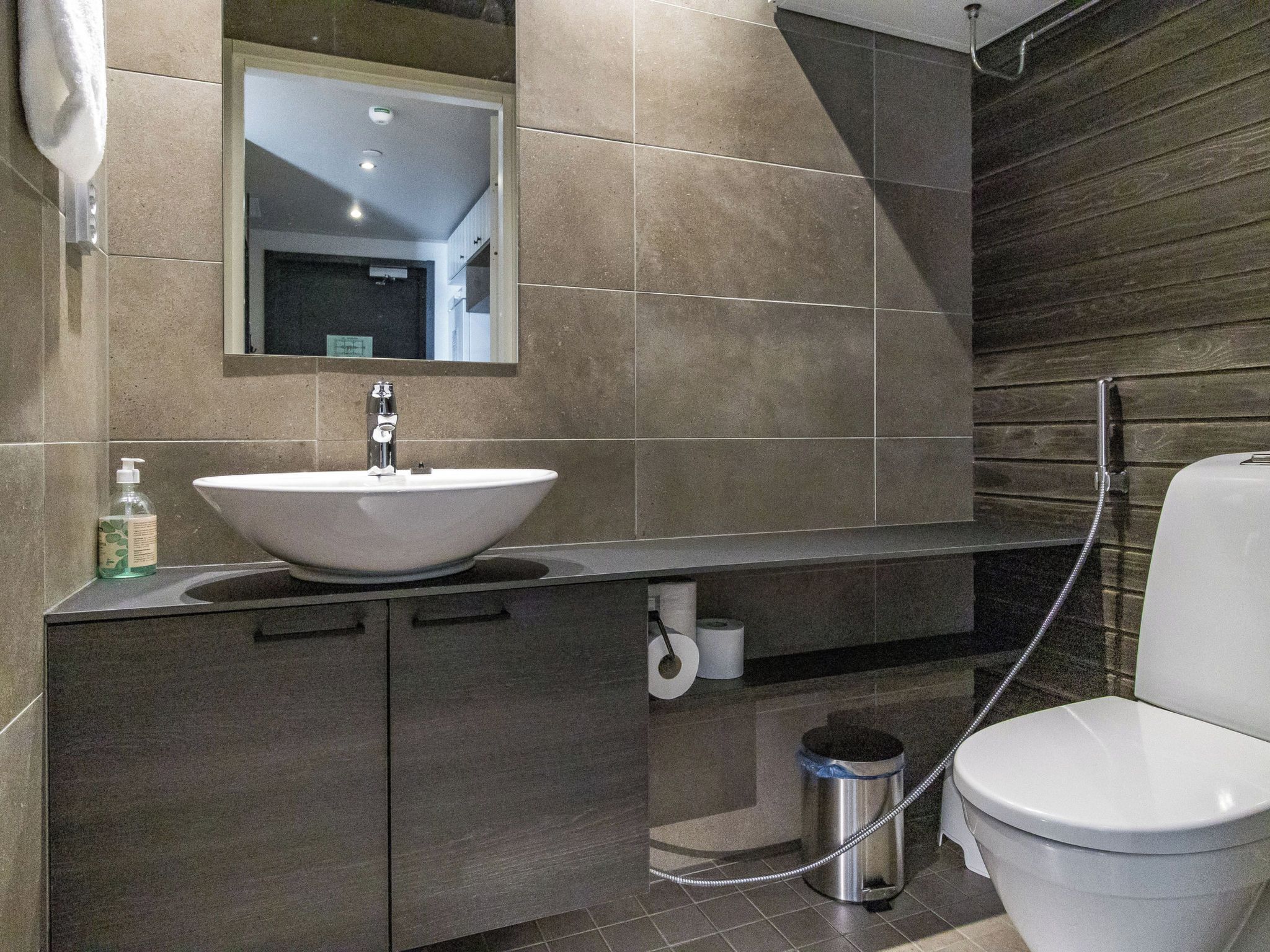 Et moderne badeværelse med vask, spejl, toilet og håndklæderække.