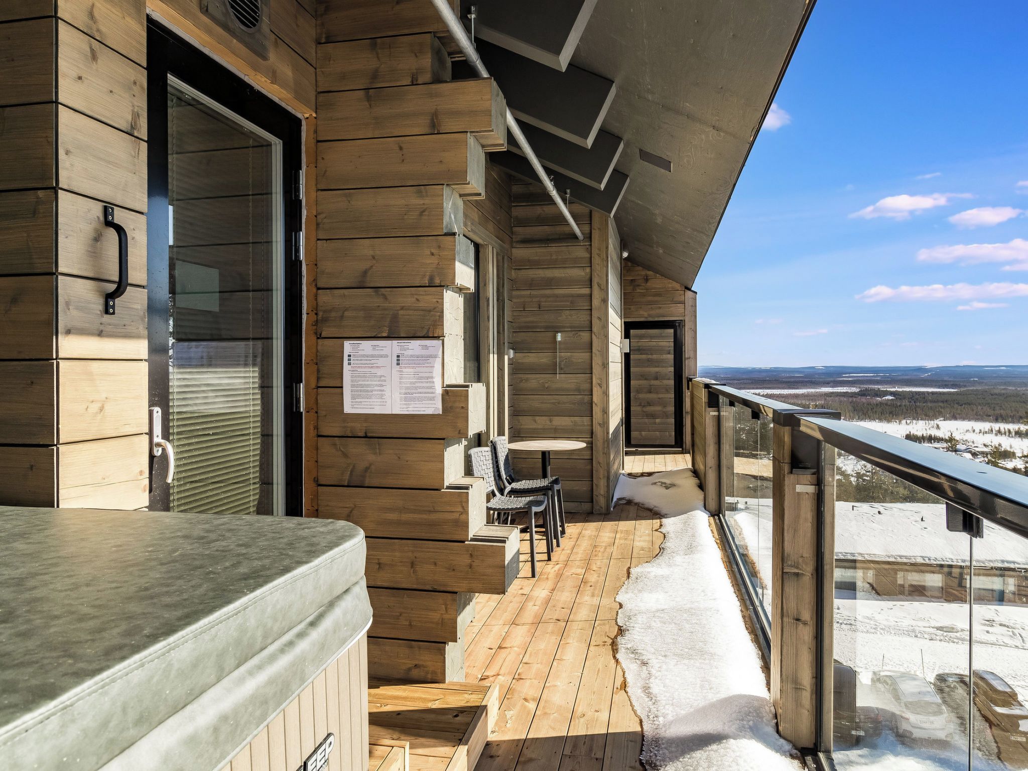A wooden deck with a hot tub, chairs, and a view of a snowy landscape.