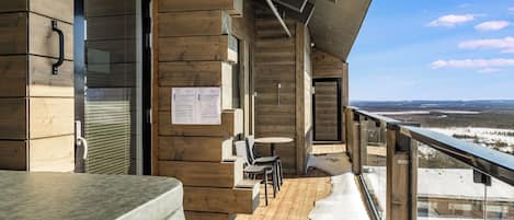 A wooden deck with a hot tub, chairs, and a view of a snowy landscape.