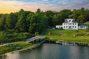 A large white house with a two-story porch and a covered bridge over a pond. - Private Estate, Guest House, Playroom, Gym, Theater | Sunny Pond by Avantstay (Austerlitz)