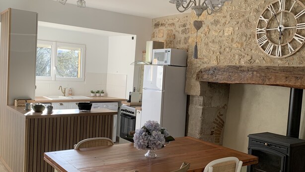 A modern kitchen with a stone wall, a wooden dining table, white chairs, and a large clock.