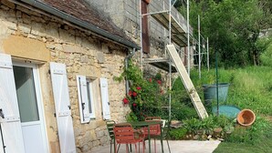 A stone building with a tiled patio, a table with chairs, and a grassy area.