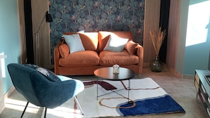 A living room with a sofa, a coffee table, a blue armchair, and a patterned wall.
