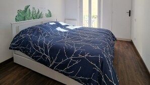 Un dormitorio con una cama, paredes blancas, una ventana y una puerta.