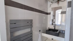 Un baño moderno con un toallero gris, un lavamanos con salpicadero estampado y un calentador blanco instalado en el techo.