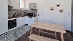 Una cocina moderna con armarios blancos, encimera de madera y horno empotrado. Hay una ventana sobre el fregadero y un estante con cristalería.
