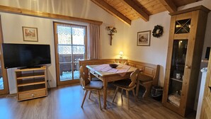 A cozy dining area with a wooden table and chairs, a television on a stand, and a window with curtains. - Ferienwohnung Zuahaisl für 4 Personen, 2 Schlafzimmer mit Balkon, 70 m² (Inzell)