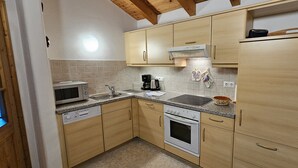 A compact kitchen with wooden cabinets, a microwave, a coffee maker, and a stove. - Ferienwohnung Zuahaisl für 4 Personen, 2 Schlafzimmer mit Balkon, 70 m² (Inzell)