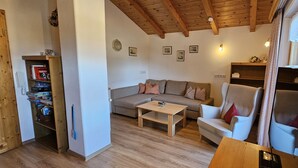 A cozy living room with a wooden ceiling, a sofa, a chair, a coffee table, and a bookshelf. - Ferienwohnung Zuahaisl für 4 Personen, 2 Schlafzimmer mit Balkon, 70 m² (Inzell)