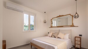 Ein Schlafzimmer mit einem großen Bett, einem Spiegel, einer Pendelleuchte und einem Fenster.