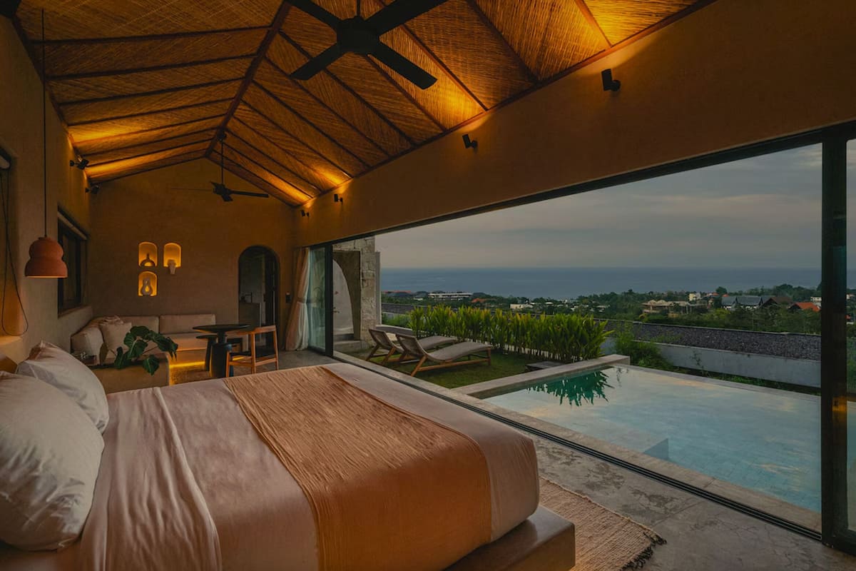 A bedroom with a large bed, a view of the ocean, a pool, and a dining area.