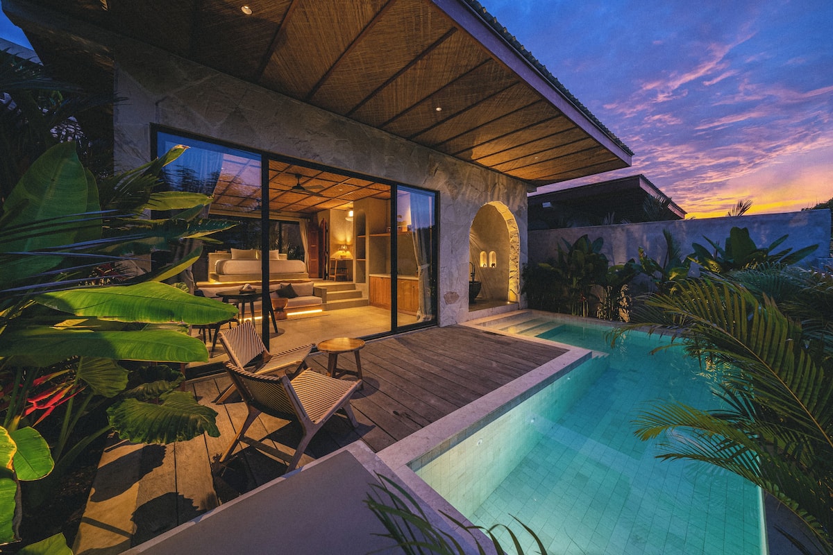 A modern house with a swimming pool, large windows, and tropical plants.