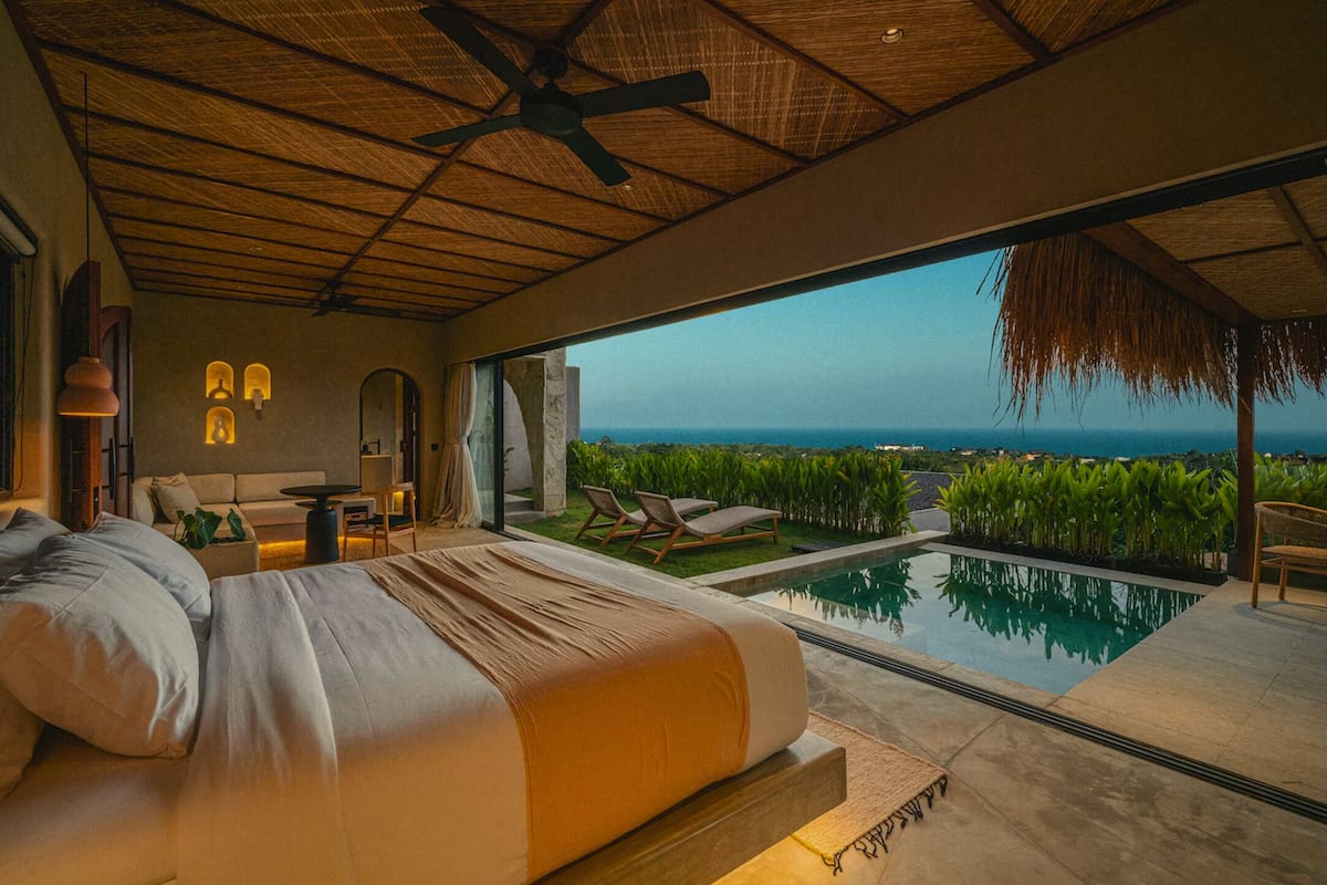 A bedroom with a large bed, a view of the ocean, a pool, and a ceiling fan.