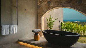 A bathroom with a large black bathtub, a stone wall, and a view of the ocean. - SIVANA, Hotel Boutique with ocean or garden views - Adults only (Pecatu)