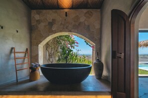 A stone-walled bathroom with a large black basin, a wooden ladder, and a view of the sea through an archway. - SIVANA, Hotel Boutique with ocean or garden views - Adults only (Pecatu)