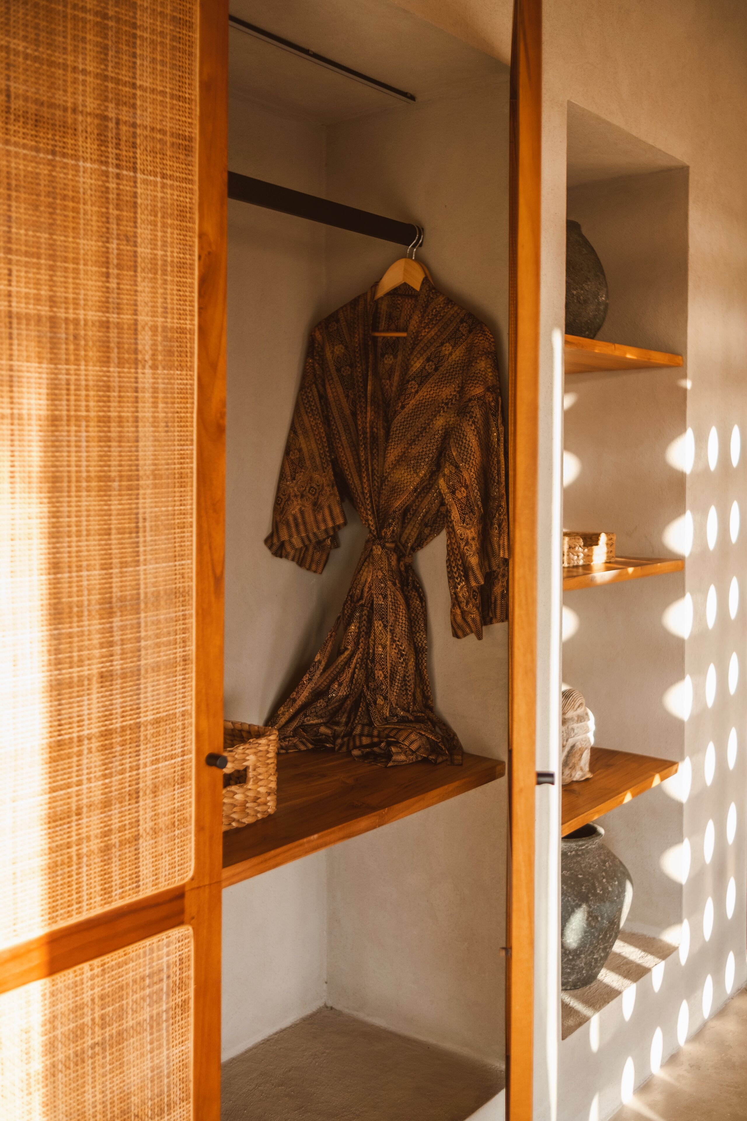 A room with a wooden wardrobe, a hanging robe, and a shelf with a vase.
