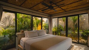 Una cama grande con cabecera, un ventilador de techo y vistas a un follaje exuberante.