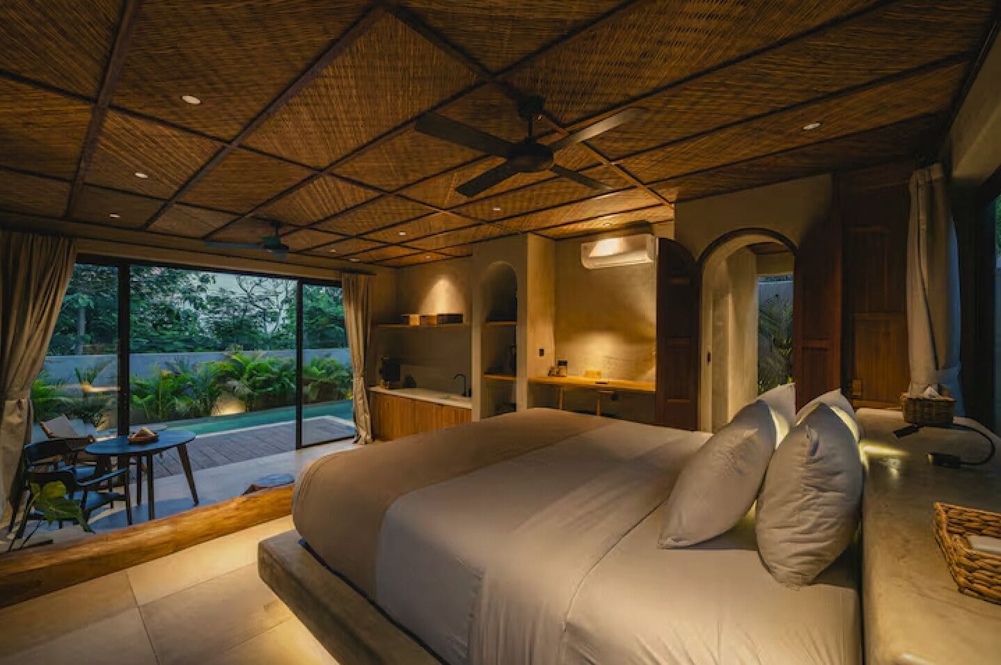 A bedroom with a large bed, a ceiling fan, and a view of a swimming pool.