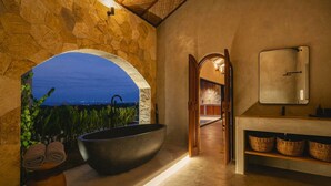 A bathroom with a large freestanding bathtub, a vanity with a mirror, and a view through an arched window. - SIVANA, Hotel Boutique with ocean or garden views - Adults only (Pecatu)
