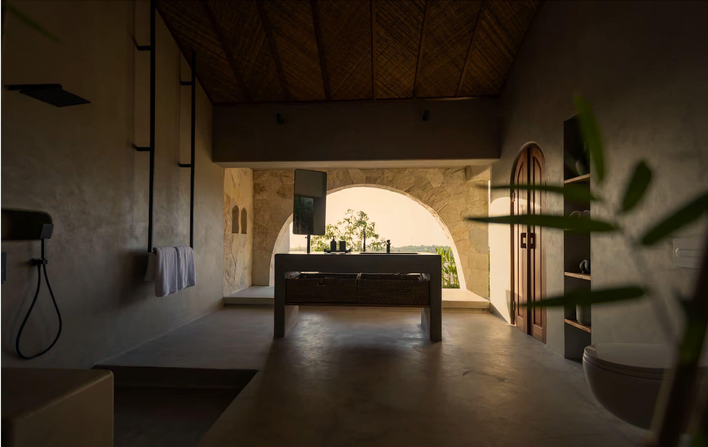 A bathroom with a stone archway, a bench, a toilet, and a shower area.