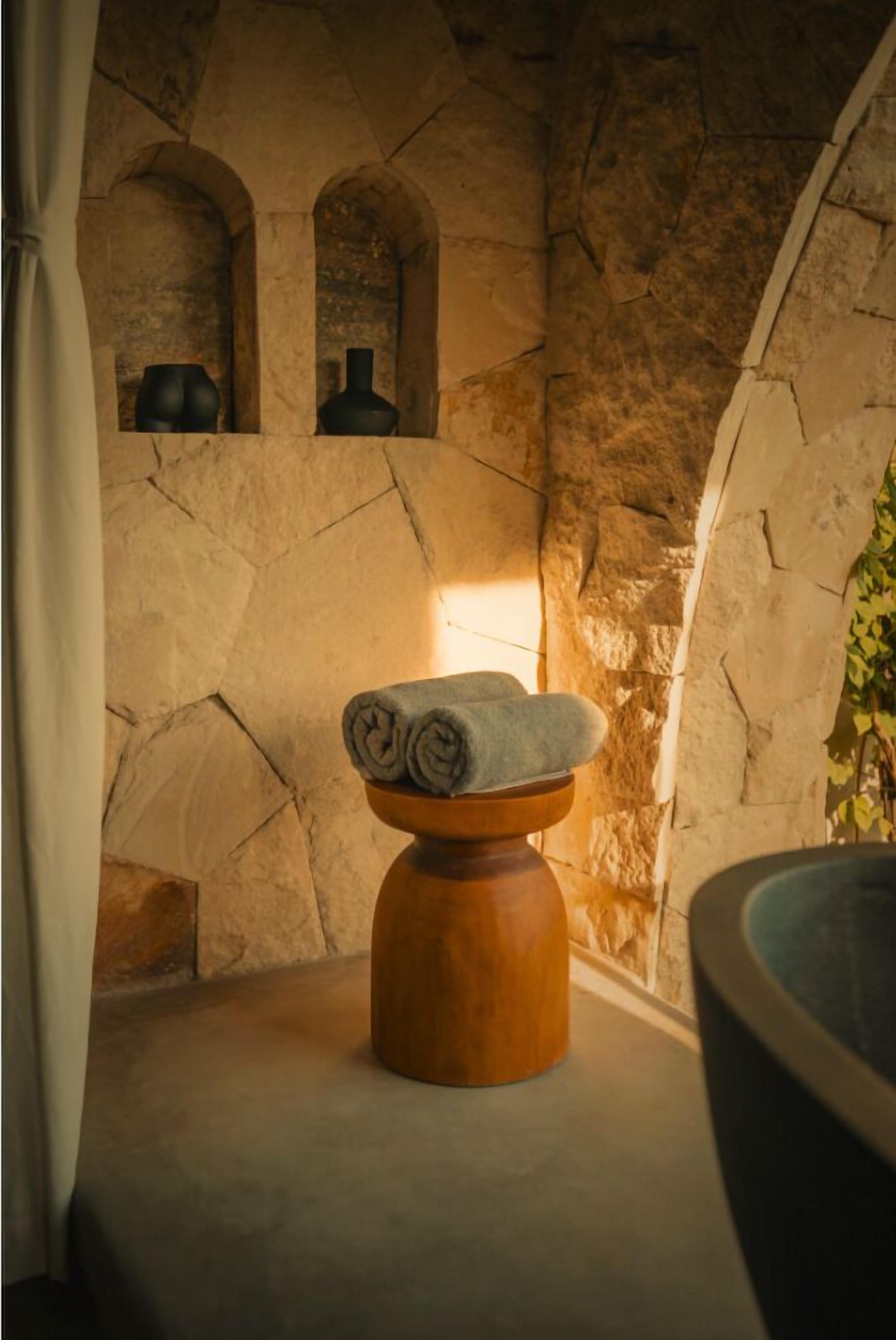 A stone-walled bathroom with a wooden stool, a bowl, and a large basin.