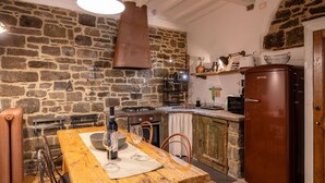 A rustic kitchen with a stone wall, wooden table, and a vintage refrigerator.
