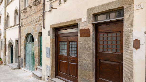 A row of stone buildings with large wooden doors, numbered plaques, and a small potted plant on the ground.