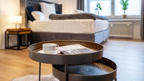 Un dormitorio moderno con una cama, una mesita de noche con una lámpara y una ventana con plantas.