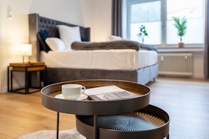 A modern bedroom with a bed, bedside table with a lamp, and a window with plants.
