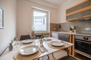 A modern kitchen with a dining area set for four. It includes a dishwasher, oven, and a window with a view of buildings.