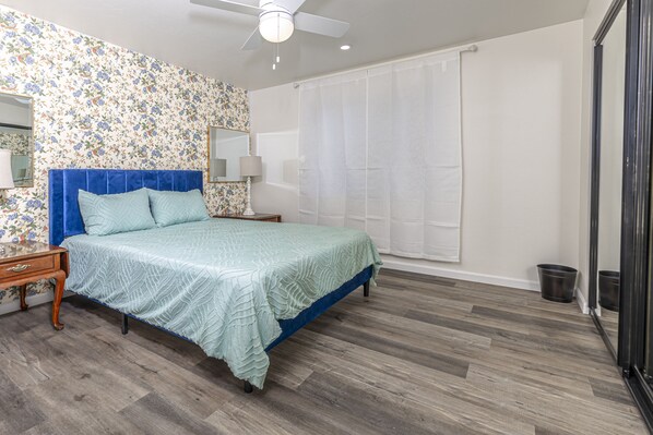 A bedroom with a bed, a nightstand, a lamp, a ceiling fan, a window with curtains, and a wooden floor. - Tranquil Green Valley Getaway, Hike, Relax & Spot Rare Birds! (Green Valley)