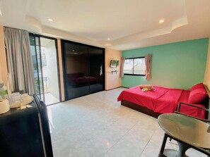 A hotel room with a bed, a table, a TV, and a sliding door leading to a balcony. - Apartment X5 (Pattaya)