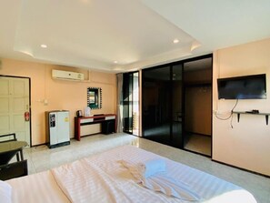 A hotel room with a bed, a desk, a refrigerator, a television, and a sliding door to a balcony. - Apartment X5 (Pattaya)