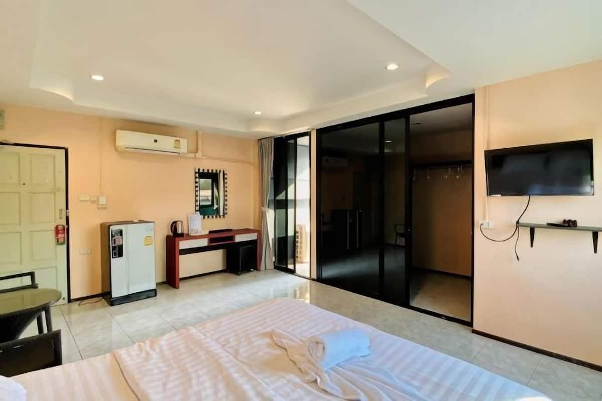 A hotel room with a bed, a desk, a chair, a television, and a sliding door leading to a balcony.